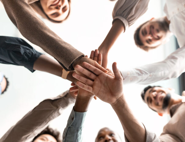 Teambuilding, Teamwork And Unity Concept. Below view of diverse group of smiling people putting their hands together, standing in circle. Multiethnic colleagues celebrating collaboration and alliance